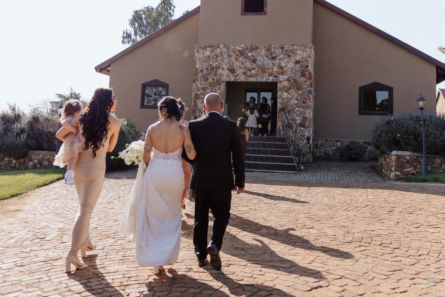 Bride walking to the chapel with her father, bridesmaid, and flower girl before the ceremony at Lezar Opstal Wedding Venue Heidelberg
